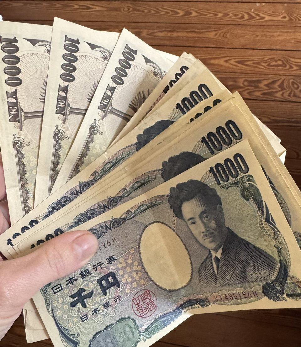 Un éventail de billets en yens japonais, 1 000 et 10 000 yens, tenu dans une main