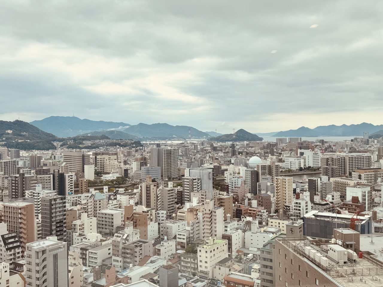 Au-dessus de Hiroshima : panorama de la ville sous les nuages, avec les montagnes et la mer en arrière-plan