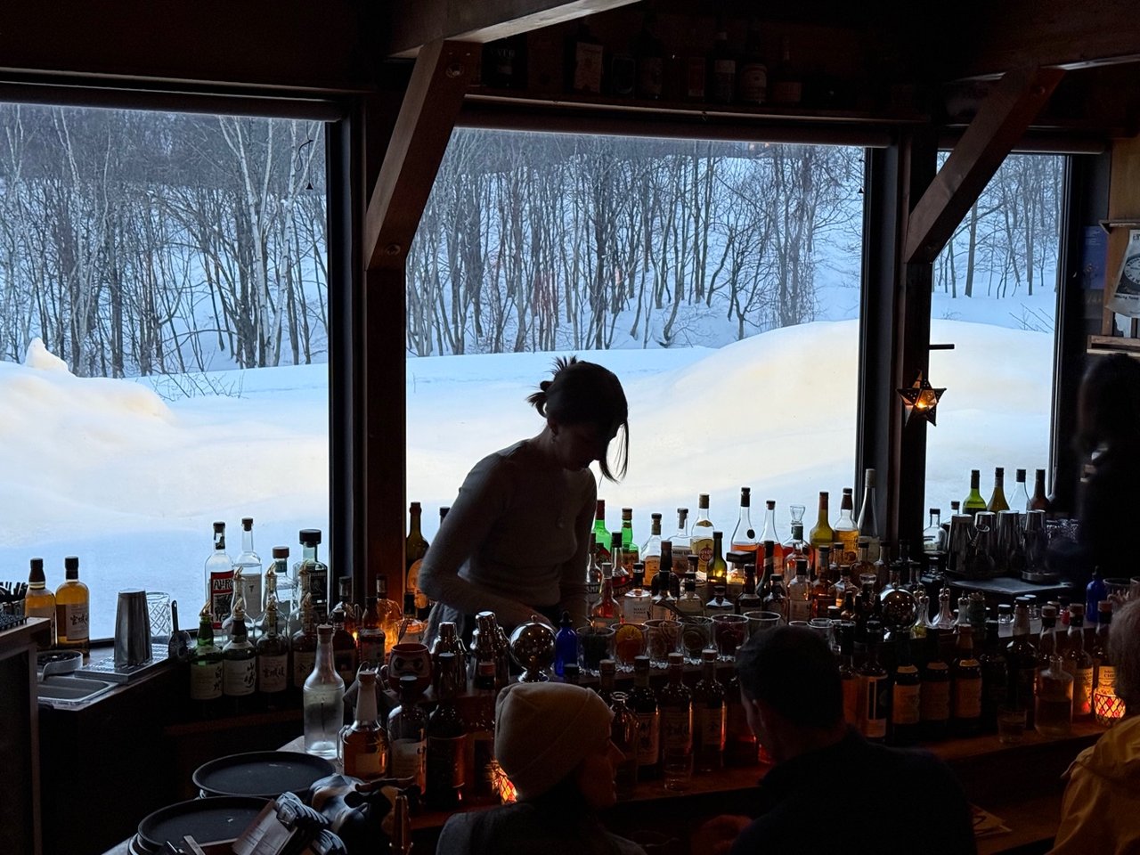 À l'intérieur du Bar Gyu à Niseko : le comptoir au crépuscule, la neige amoncelée contre les fenêtres