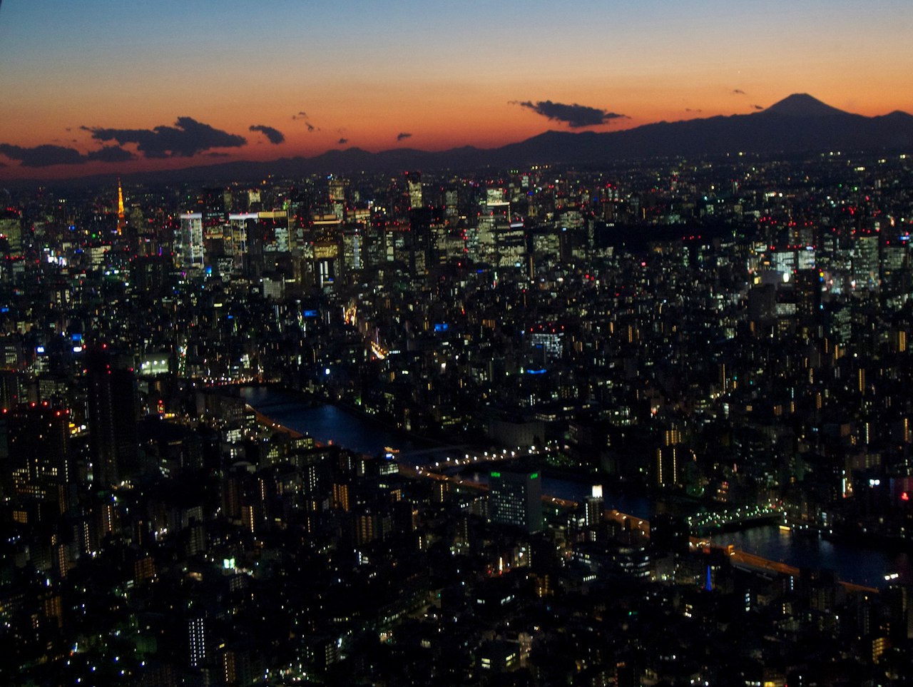 Tokyo au crépuscule vu d'en haut, les lumières de la ville qui s'allument, la tour de Tokyo à gauche et le mont Fuji à l'horizon