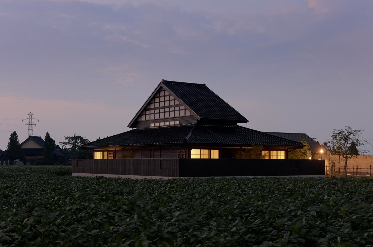 Rakudo-an à Toyama au crépuscule : un ryokan en bois sombre aux lumières chaudes, photographié depuis l’autre côté des champs