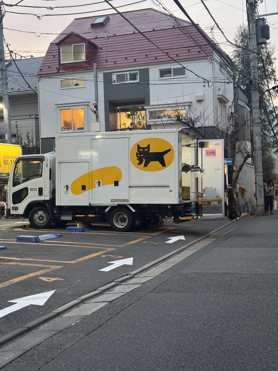 A Yamato Transport delivery truck with the black cat logo, back doors open on a city street at dusk