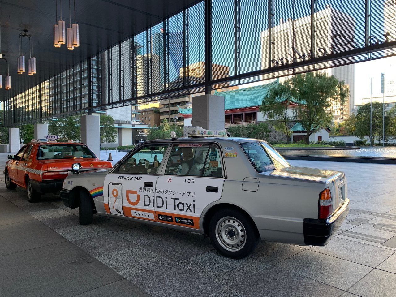 Des taxis attendant sous l’auvent d’un hôtel de Tokyo, un DiDi Taxi devant
